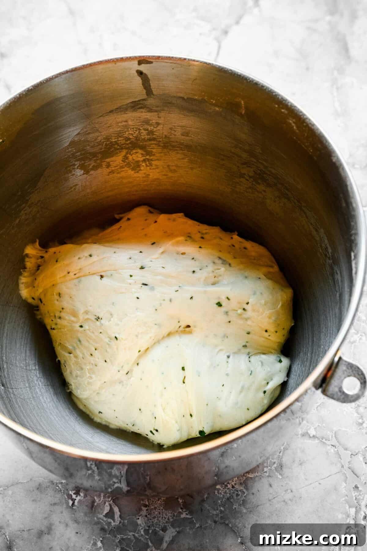 These easy garlic herb parker house rolls are buttery, moist, and tender, and the perfect side for a Thanksgiving or Christmas meal. A stand mixer with freshly kneaded garlic and herb roll dough inside.