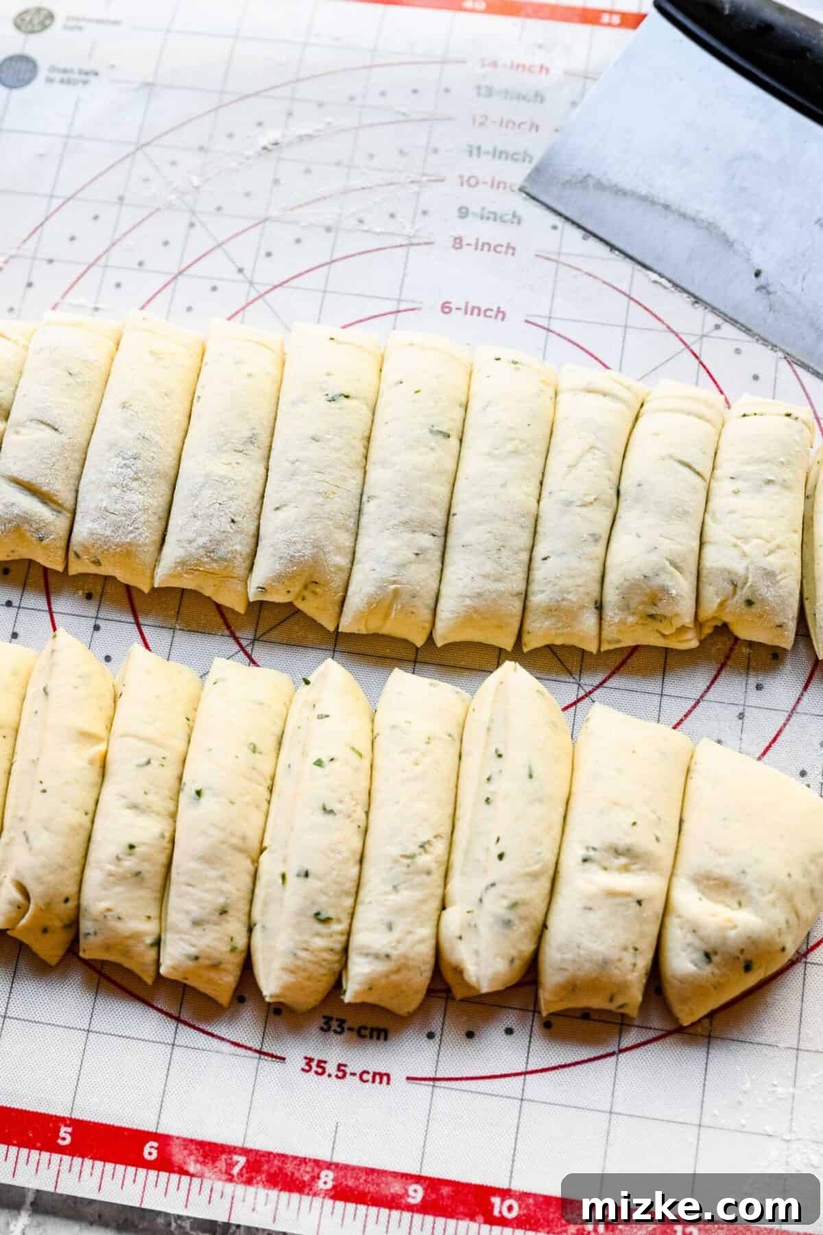 These easy garlic herb parker house rolls are buttery, moist, and tender, and the perfect side for a Thanksgiving or Christmas meal. Close-up view of two perfectly portioned logs of garlic herb parker house roll dough, positioned next to a stand mixer.
