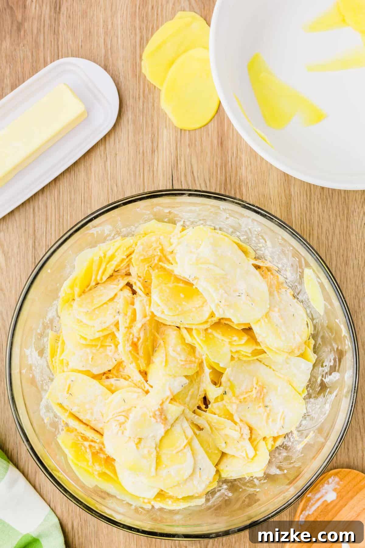 Simply Irresistible Creamy Potato Gratin 8 Thinly sliced potatoes fully coated in a creamy cheese mixture within a clear mixing bowl, ready for layering.