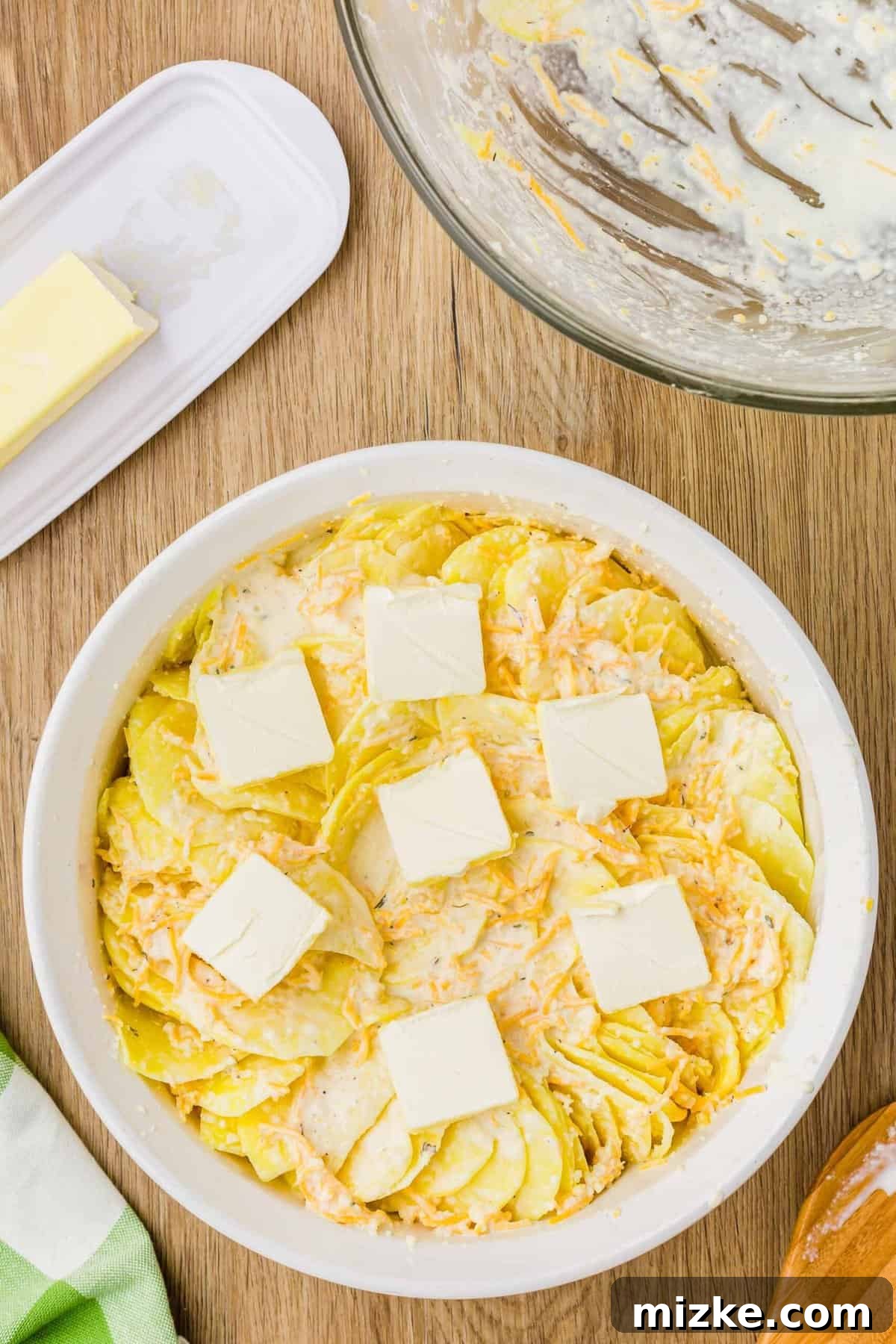 Simply Irresistible Creamy Potato Gratin 10 Thinly sliced potato layers meticulously arranged in a baking dish, adorned with small pads of butter slices on top, ready for the oven.