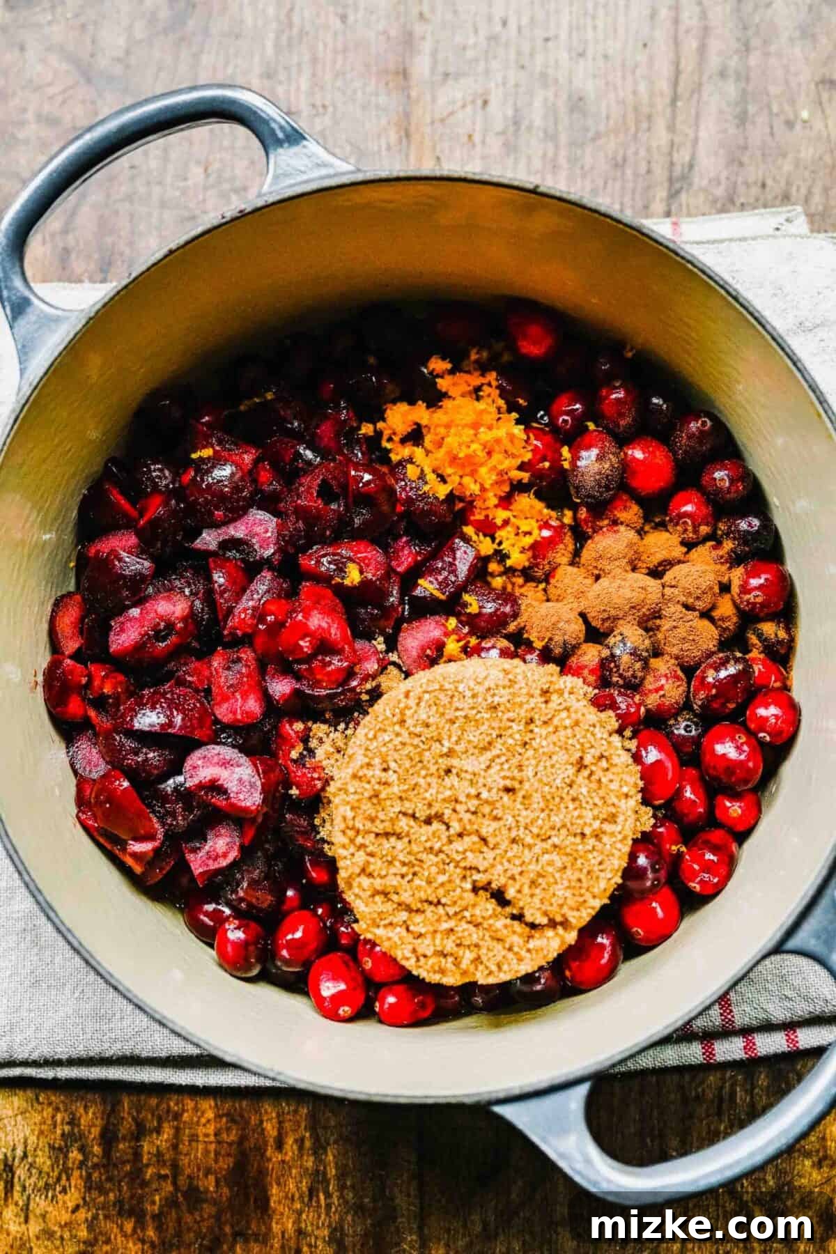 This cranberry cherry compote recipe is tart and sweet, takes only 25 minutes to make, and can be made in advance for any Thanksgiving meal. Cranberries and cherries in a pot, with brown sugar and orange zest on top