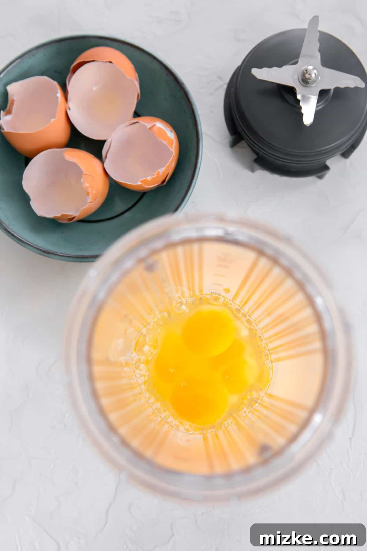 Fluffy Instant Pot Egg Bites 6 Overhead shot of eggs in a blender jar next to egg shells and blender blade, ready for blending.