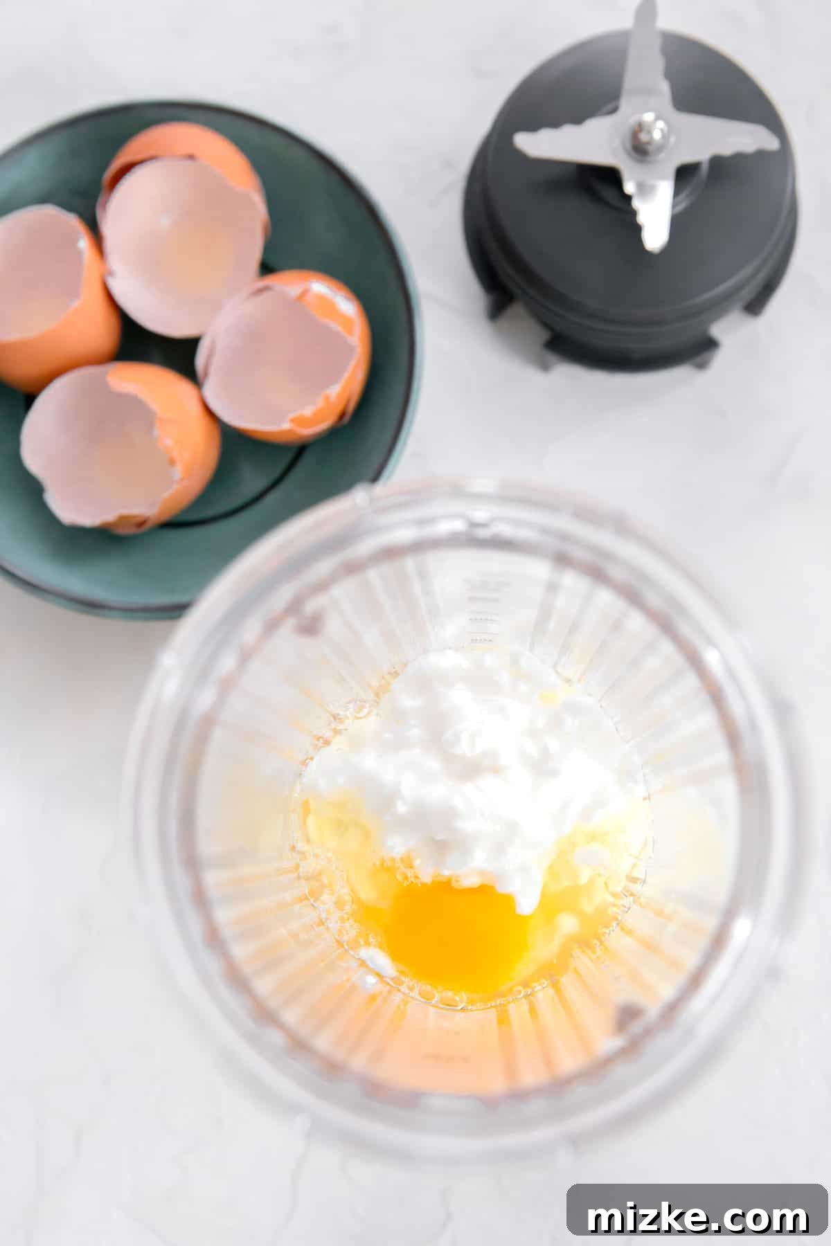 Fluffy Instant Pot Egg Bites 7 Overhead shot of eggs and cottage cheese in a blender jar next to egg shells and blender blade, showcasing the next ingredient addition.
