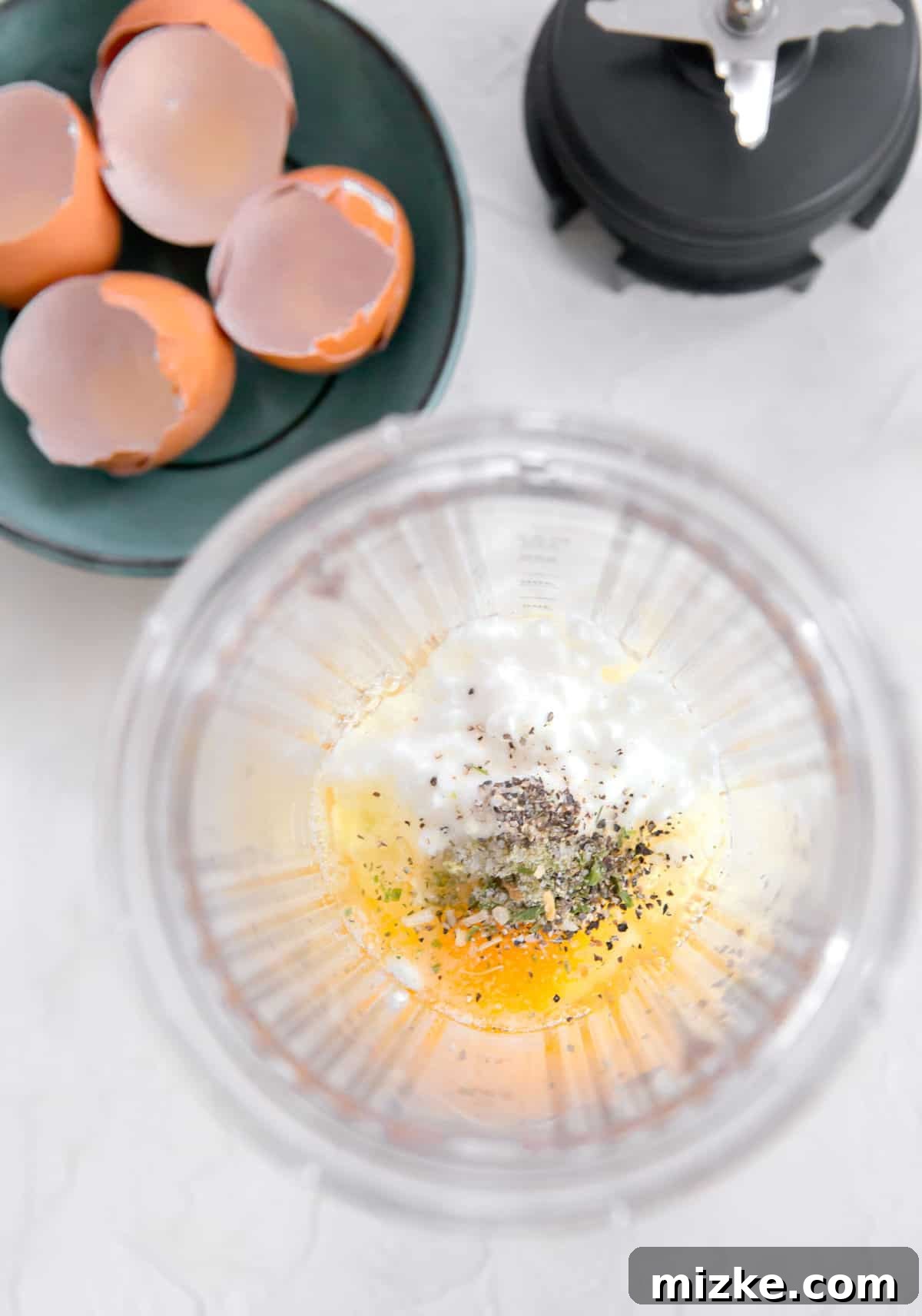 Fluffy Instant Pot Egg Bites 8 Overhead shot of eggs, cottage cheese, and seasonings in a blender jar next to egg shells and blender blade, showing all ingredients combined before blending.