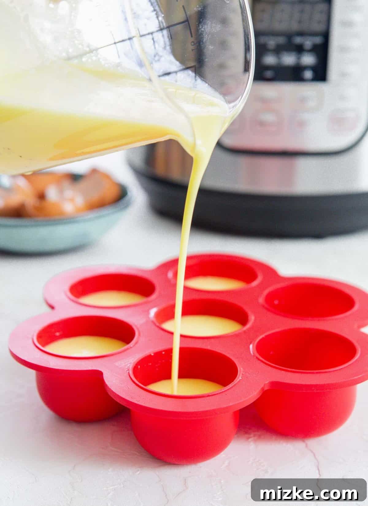 Fluffy Instant Pot Egg Bites 9 Egg mixture in a clear container being poured into a red egg mold in front of an Instant Pot and blue plate with egg shells, illustrating the filling process.