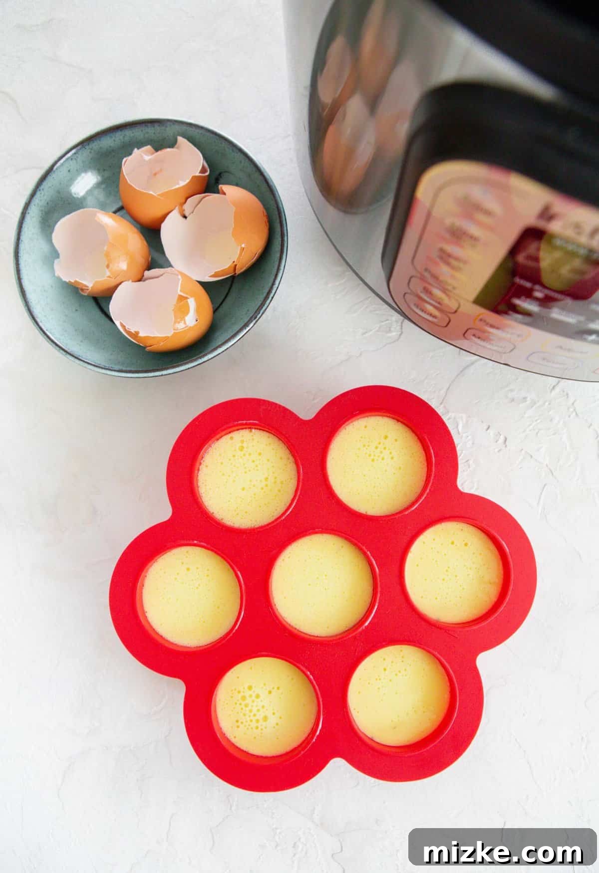 Fluffy Instant Pot Egg Bites 10 Overhead shot with filled red egg molds next to a blue plate with egg shells and an Instant Pot, showing the molds ready for cooking.