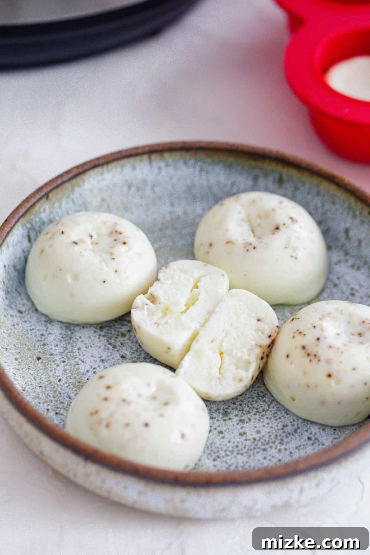 Fluffy Instant Pot Egg White Bites 10 Cooked egg white egg bites on a ceramic plate, with one bite sliced in half to reveal its airy interior.