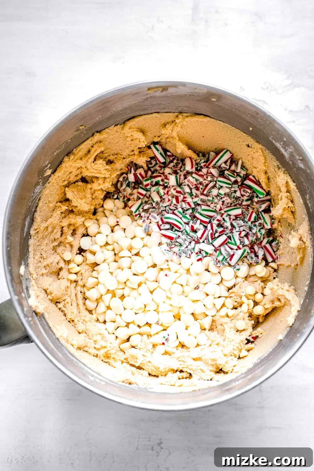 White Chocolate Peppermint Bliss Cookies 6 white chocolate chips and crushed candy canes sitting on top of the cookie dough in a metal bowl