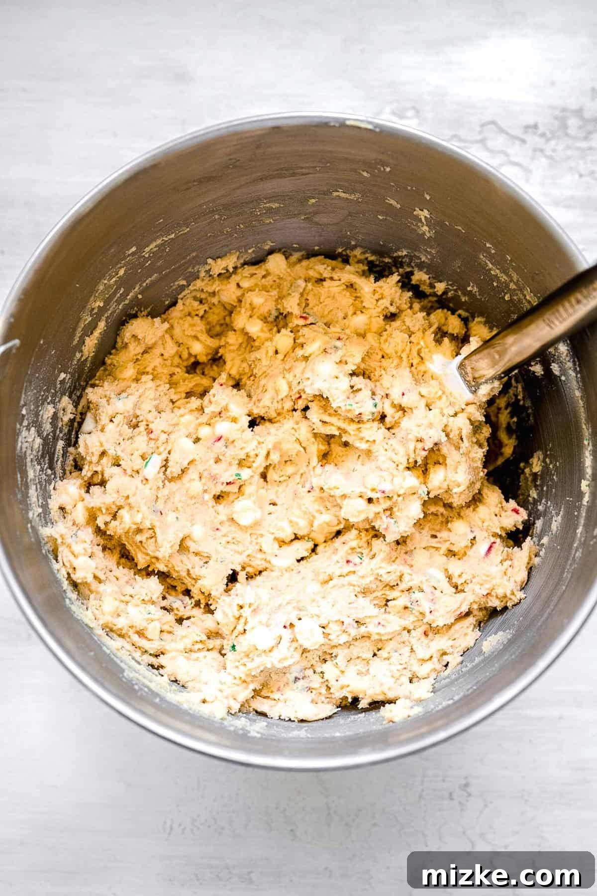 White Chocolate Peppermint Bliss Cookies 7 white chocolate chips and crushed candy canes being mixed with the dough with a spatula in a metal bowl