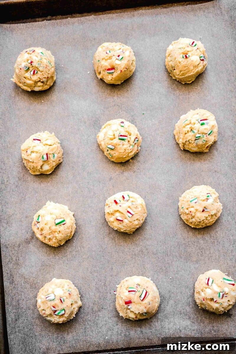 White Chocolate Peppermint Bliss Cookies 8 raw peppermint white chocolate cookie dough rolled and on top of parchment paper on a baking sheet