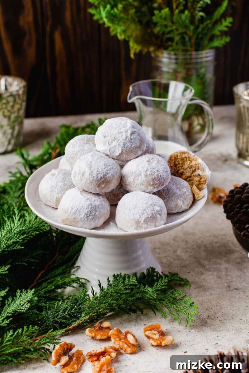 Melt-in-Your-Mouth Snowballs 3 a pile of snowball cookies stacked on top of a cake stand with evergreen leaves and pine cones in the foreground