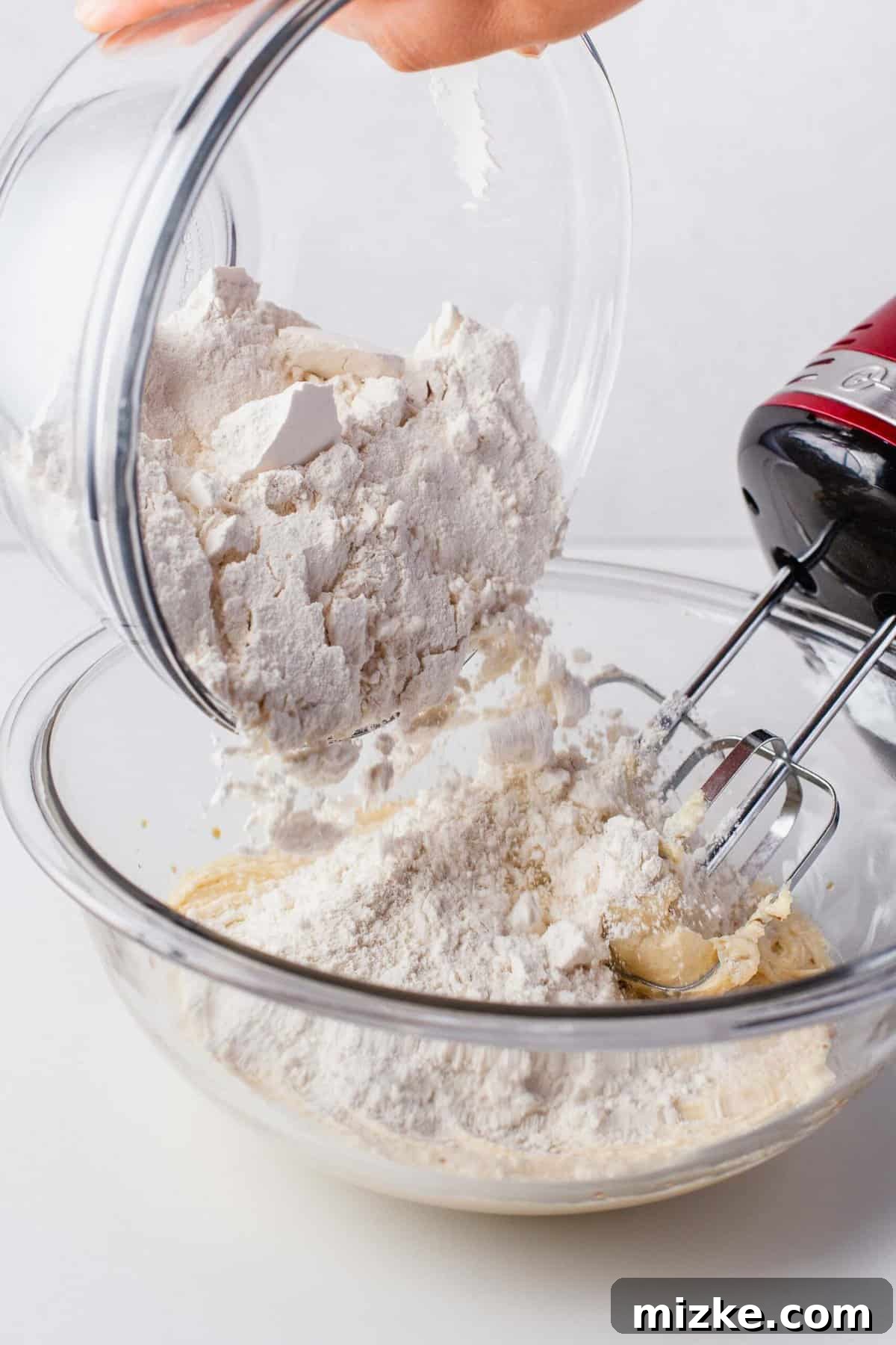 Melt-in-Your-Mouth Snowballs 6 flour being poured into a large clear bowl with creamed butter and sugar with a hand mixer in the bowl
