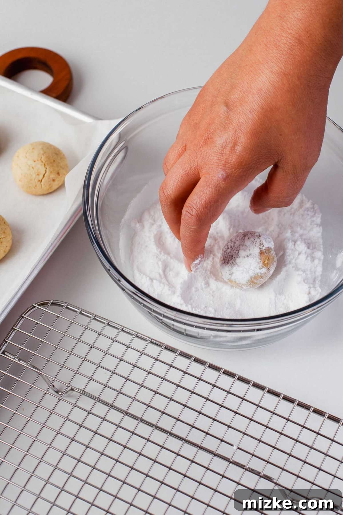 Melt-in-Your-Mouth Snowballs 9 a hand in a bowl of powdered sugar rolling the cookie in it