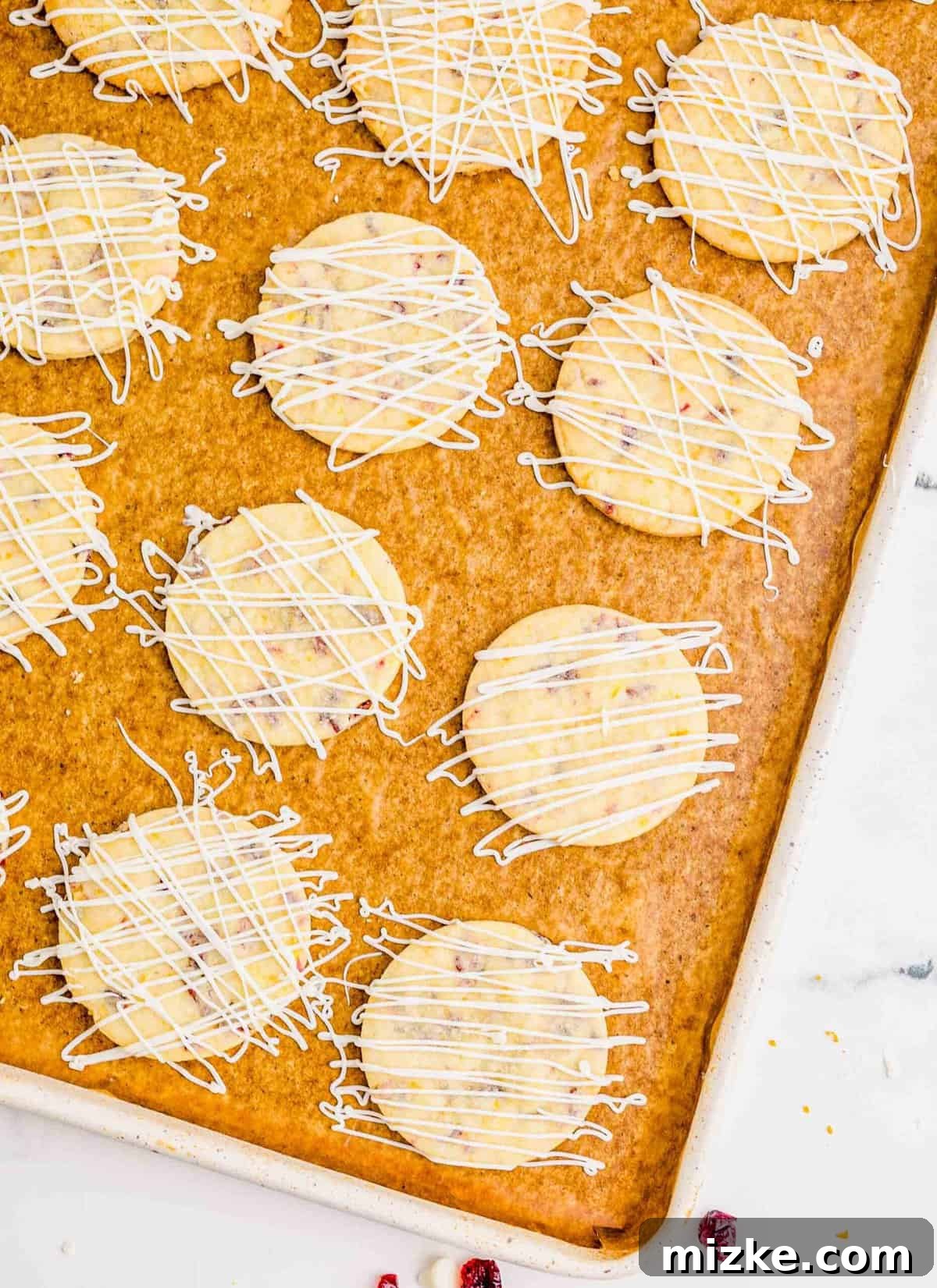 Golden Orange Cranberry Shortbread Delights 12 A large baking sheet with cranberry orange shortbread cookies finished with white chocolate drizzle on top.