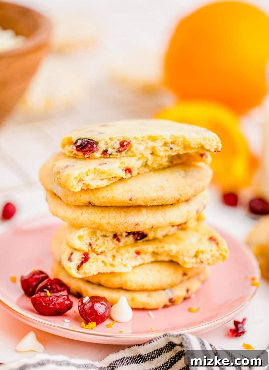 Golden Orange Cranberry Shortbread Delights 3 Cranberry orange shortbread cookies neatly stacked on a pink plate, adorned with dried cranberries and white chocolate chips.