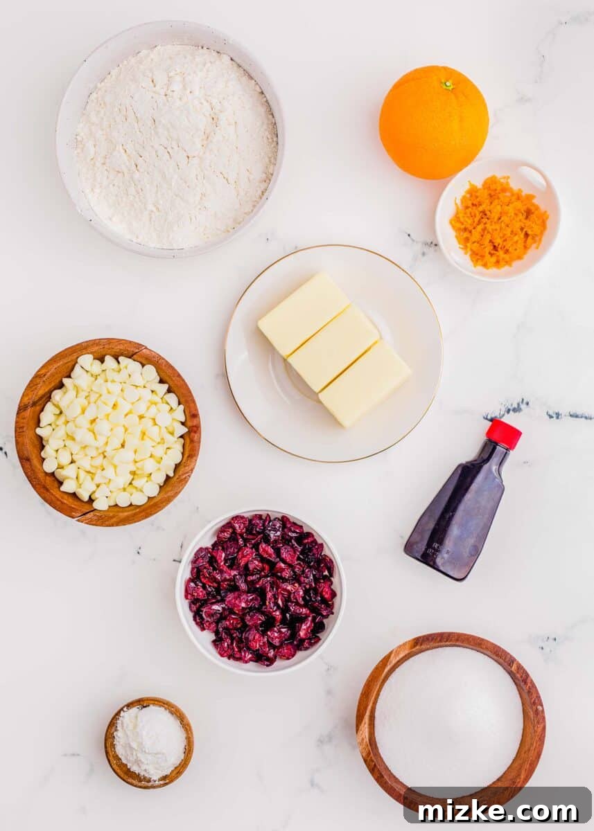 Golden Orange Cranberry Shortbread Delights 4 Ingredients for cranberry orange shortbread cookies: flour, butter, orange zest, almond extract, sugar, cornstarch, dried cranberries, and white chocolate chips laid out on a surface.