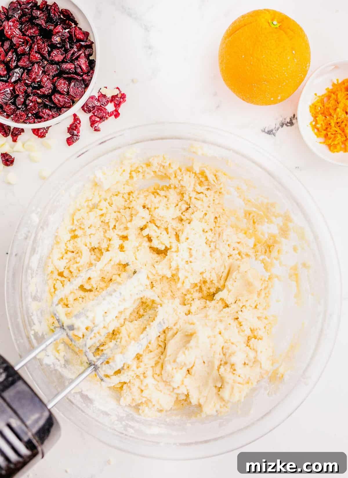 Golden Orange Cranberry Shortbread Delights 5 Creaming together butter and sugar in a large clear bowl next to an orange and orange zest.