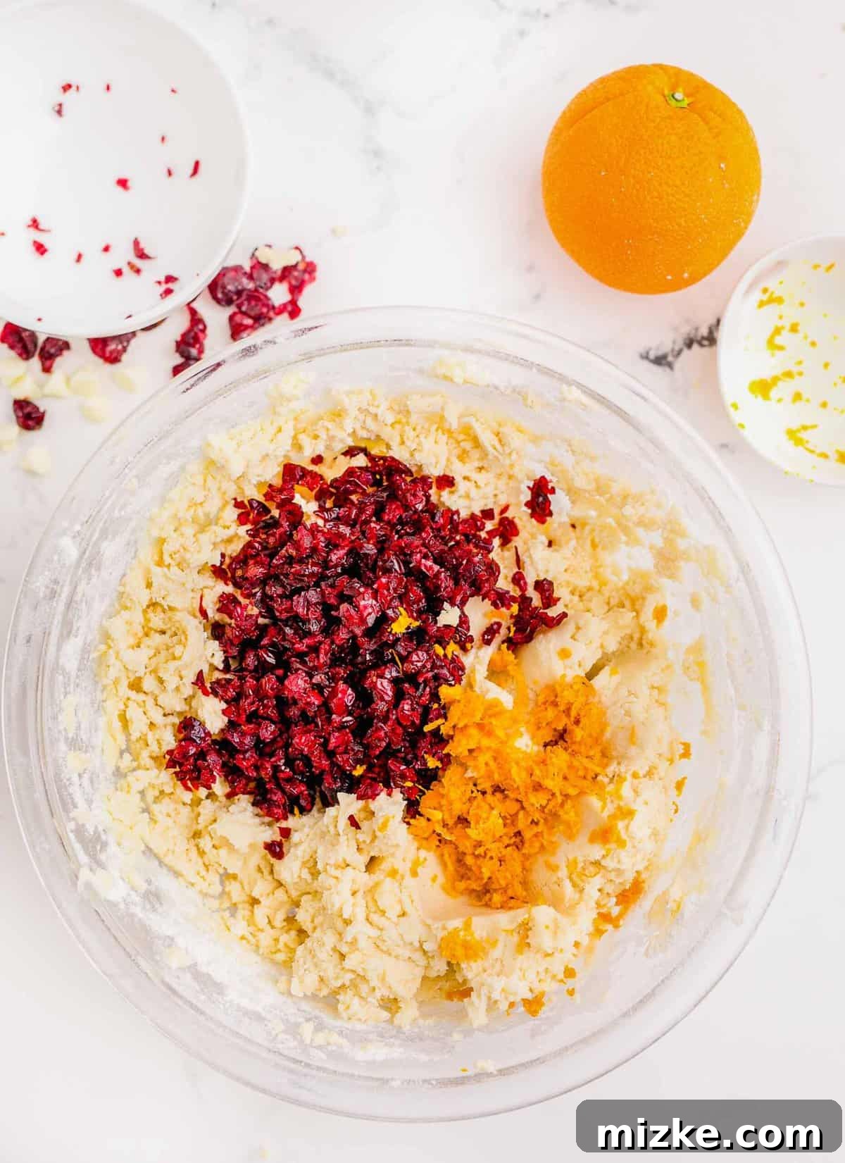 Golden Orange Cranberry Shortbread Delights 7 Dried cranberries and orange zest added to shortbread cookie dough in a large clear bowl.