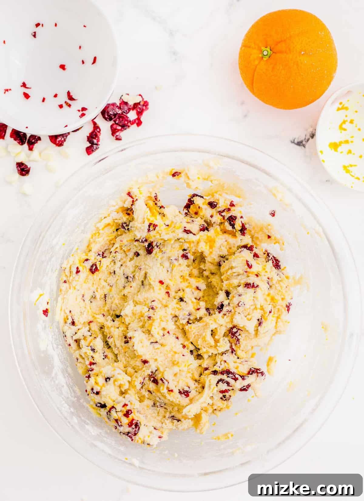 Golden Orange Cranberry Shortbread Delights 8 Cranberry orange shortbread cookie dough mixed with dried cranberries and orange zest in a large clear bowl next to an orange.