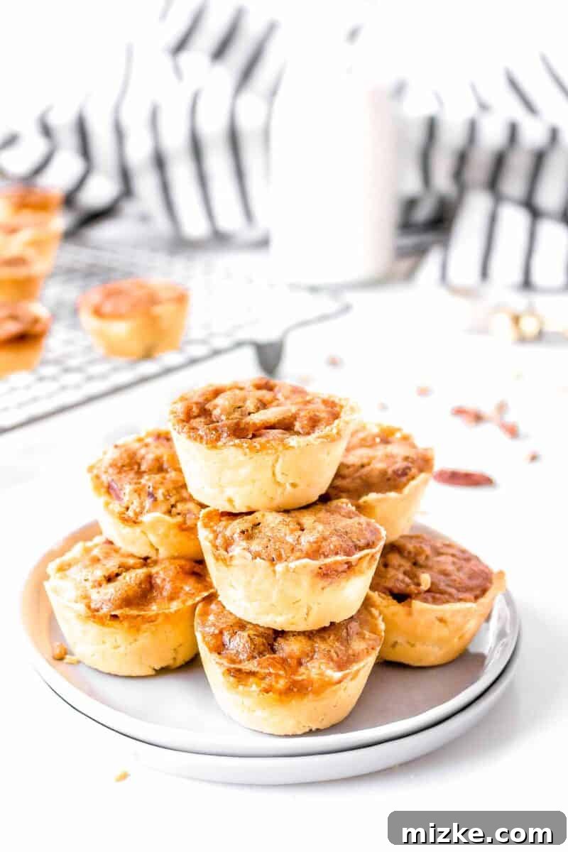 Effortless Pecan Tassie Bites 12 A stack of golden pecan tassies on two grey plates, with a rustic jar of milk and striped linen in the soft background, ready for serving.