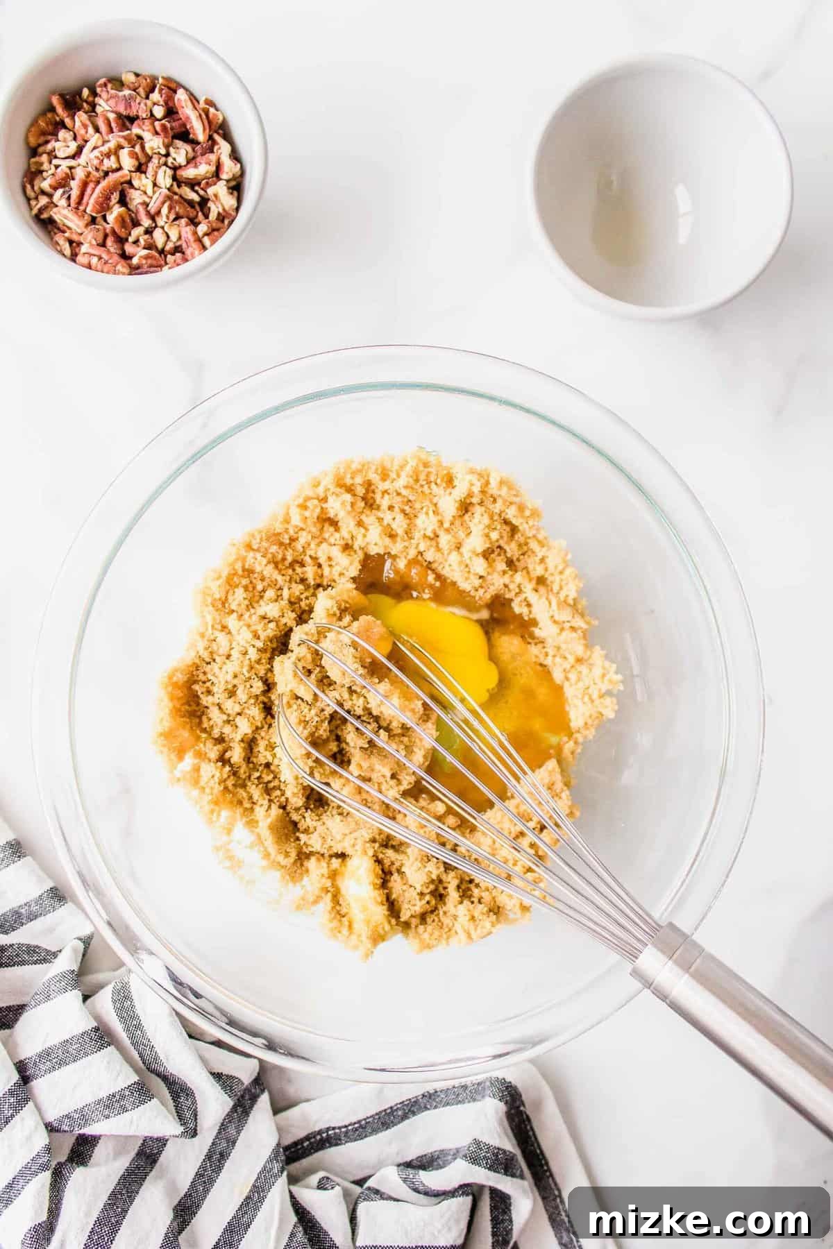 Effortless Pecan Tassie Bites 7 Whisking together brown sugar, a fresh egg, melted butter, and fragrant vanilla extract in a clear bowl to create the rich pecan filling, next to a striped linen towel.