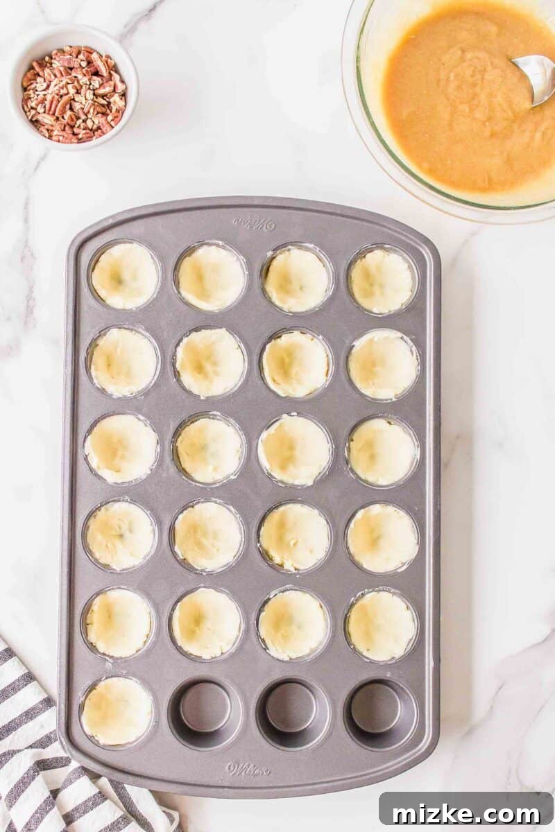Effortless Pecan Tassie Bites 8 Tender cream cheese dough meticulously pressed into the cups of a mini muffin pan, forming the perfect base for pecan tassies.