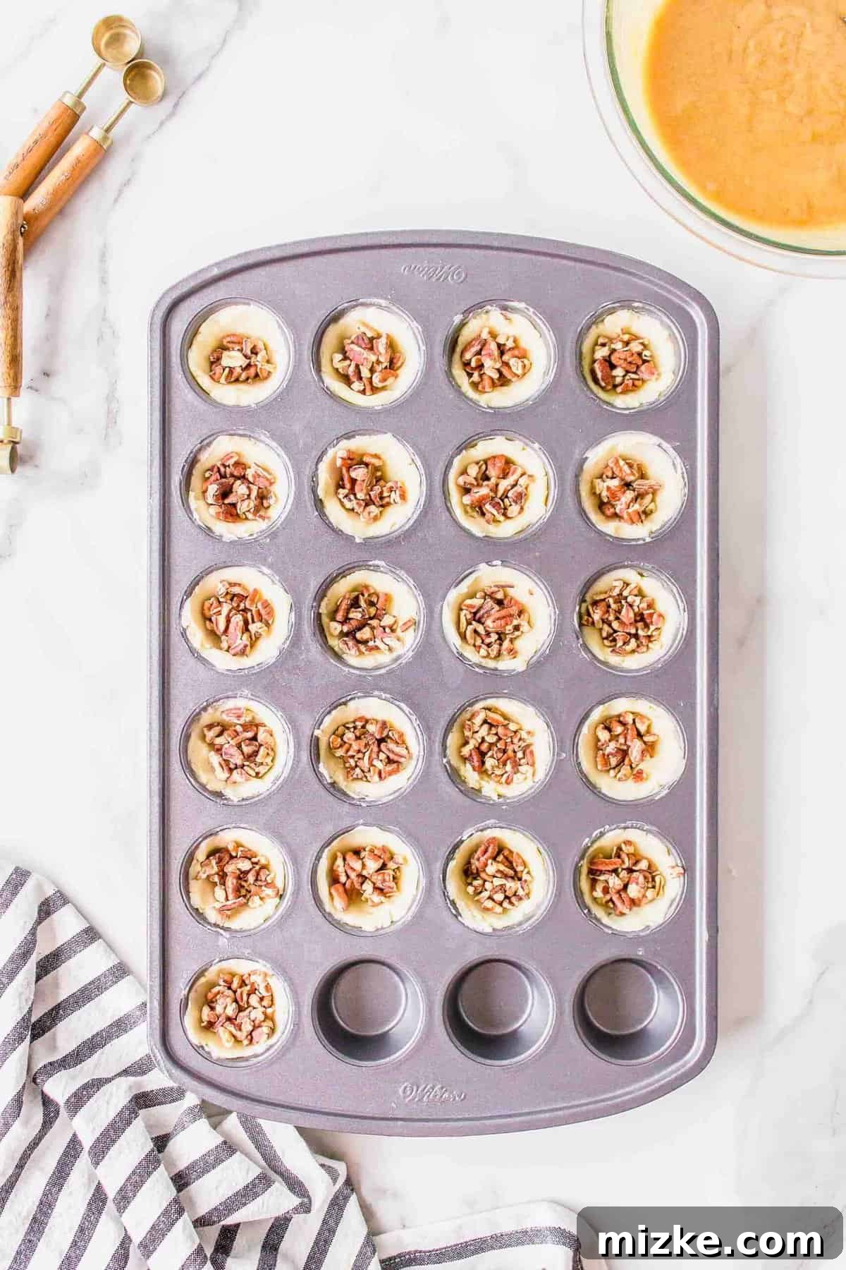 Effortless Pecan Tassie Bites 9 Coarsely chopped pecans being carefully divided and added into the pre-formed dough cups within the mini muffin pan.