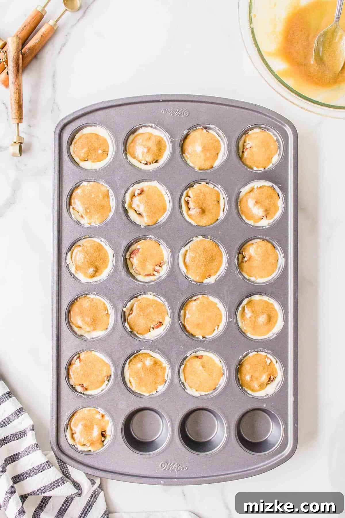 Effortless Pecan Tassie Bites 10 The sweet, eggy pecan pie filling being spooned on top of the chopped pecans in each mini dough cup of the muffin pan.