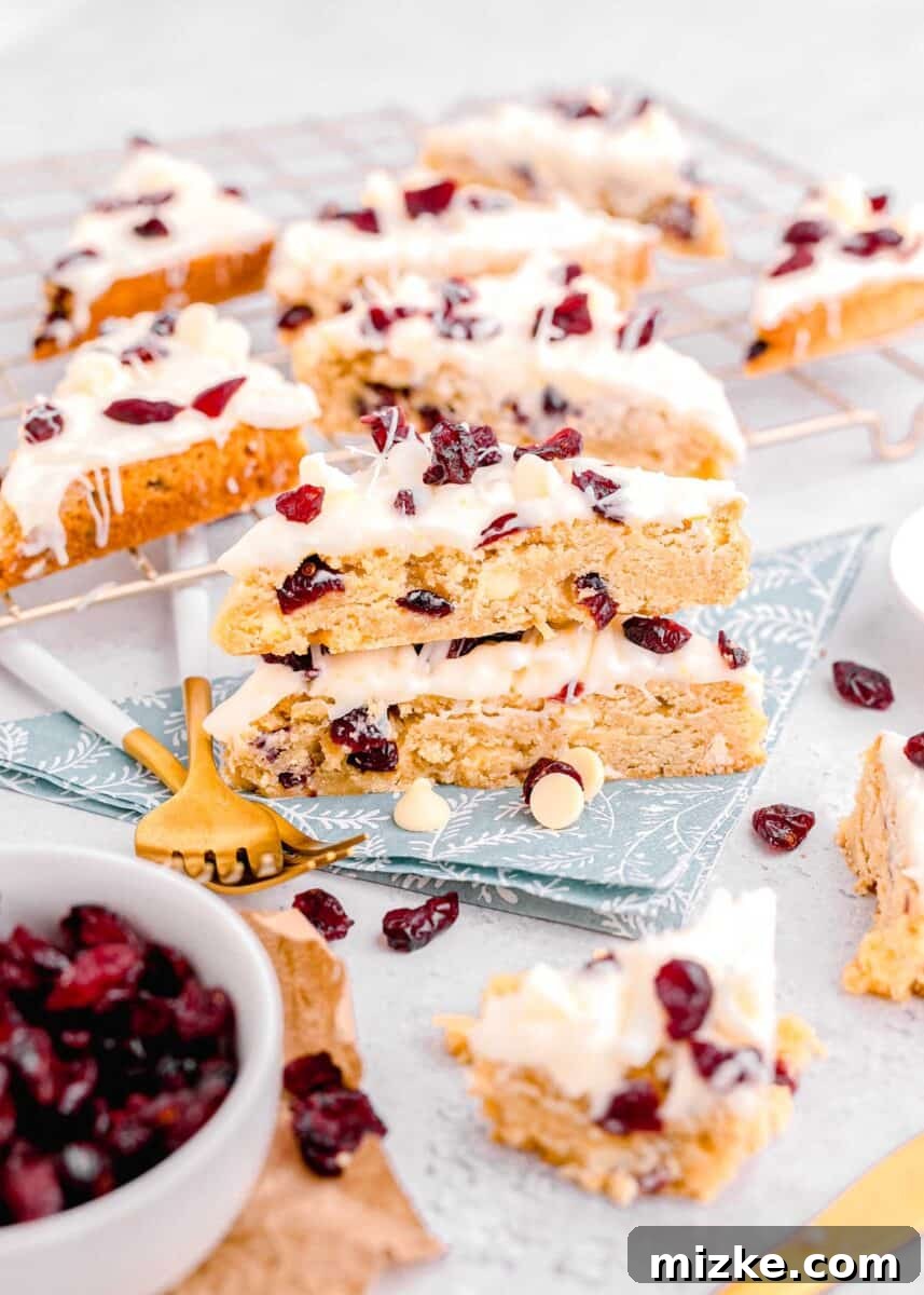 Bake Your Own Cranberry Bliss 2 Stacked homemade cranberry bliss bars on a blue floral towel, with more bars in the background on a metal baking rack.