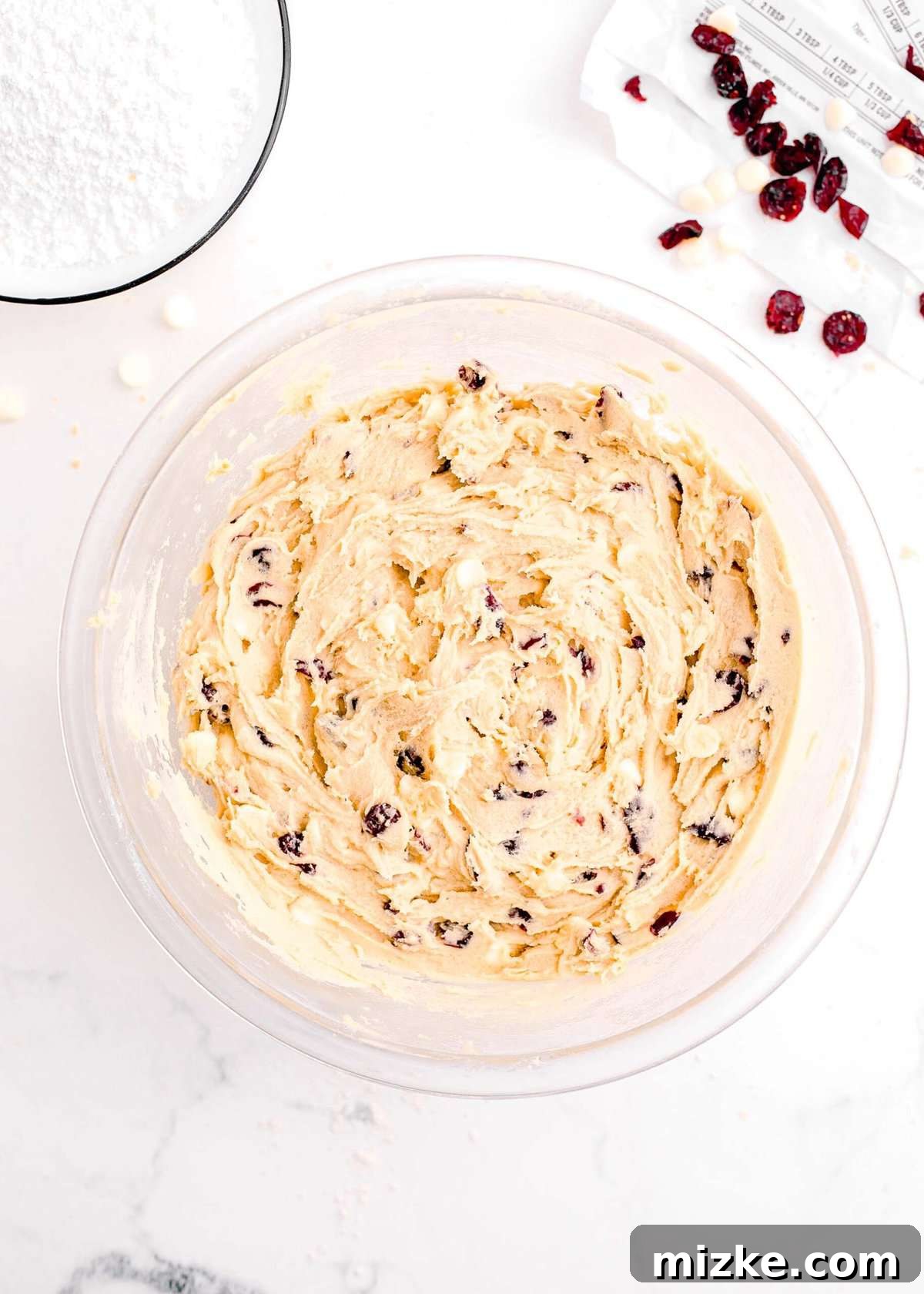 Bake Your Own Cranberry Bliss 11 The completed cranberry bliss bar dough, with white chocolate and dried cranberries evenly distributed, in a clear bowl.