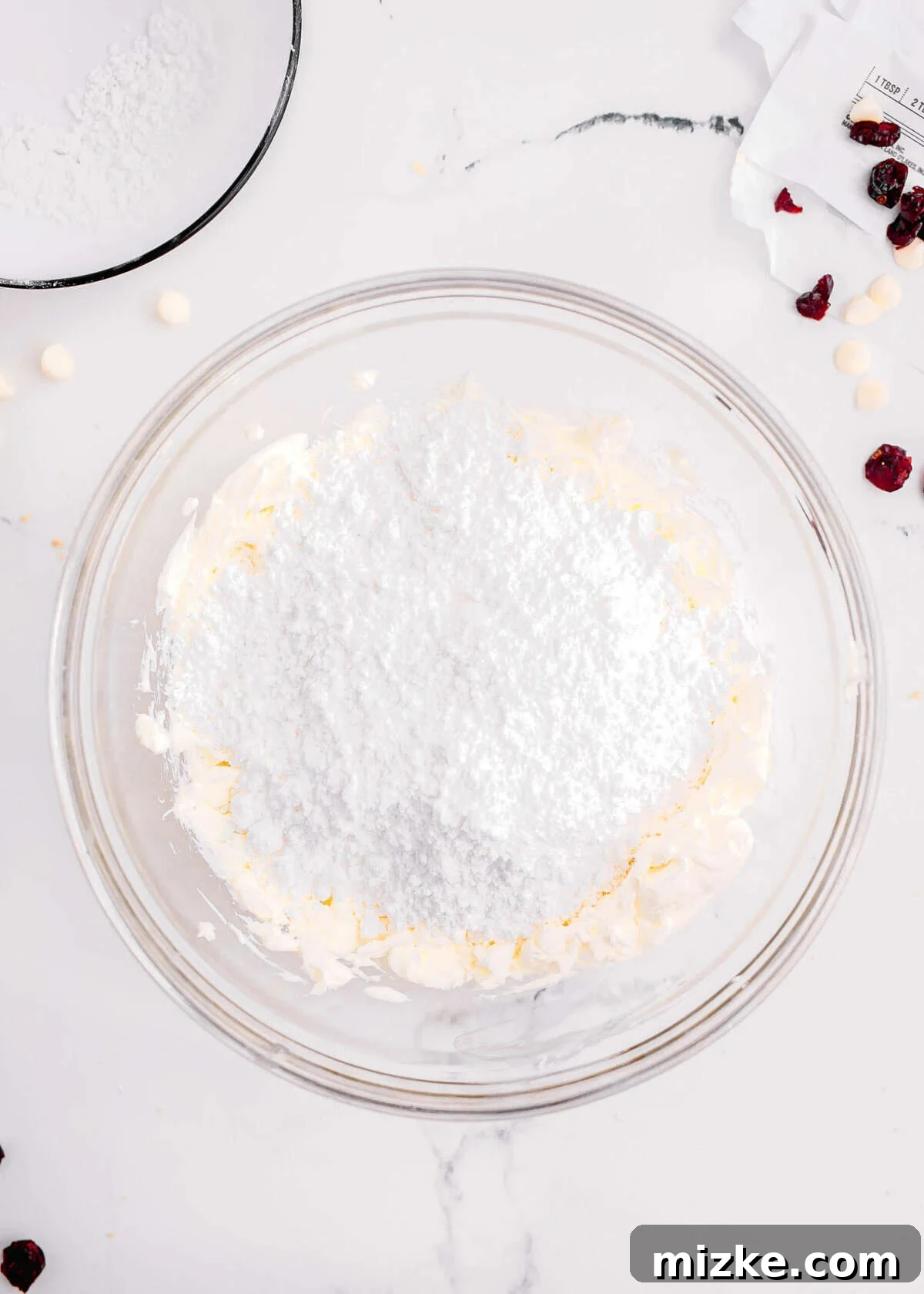 Bake Your Own Cranberry Bliss 13 Adding powdered sugar to softened cream cheese in a clear mixing bowl.
