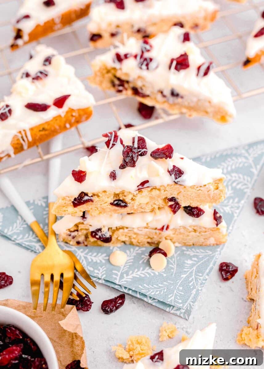 Bake Your Own Cranberry Bliss 3 Cranberry bliss bars arranged on a blue floral napkin, with a metal baking rack holding more bars in the background.