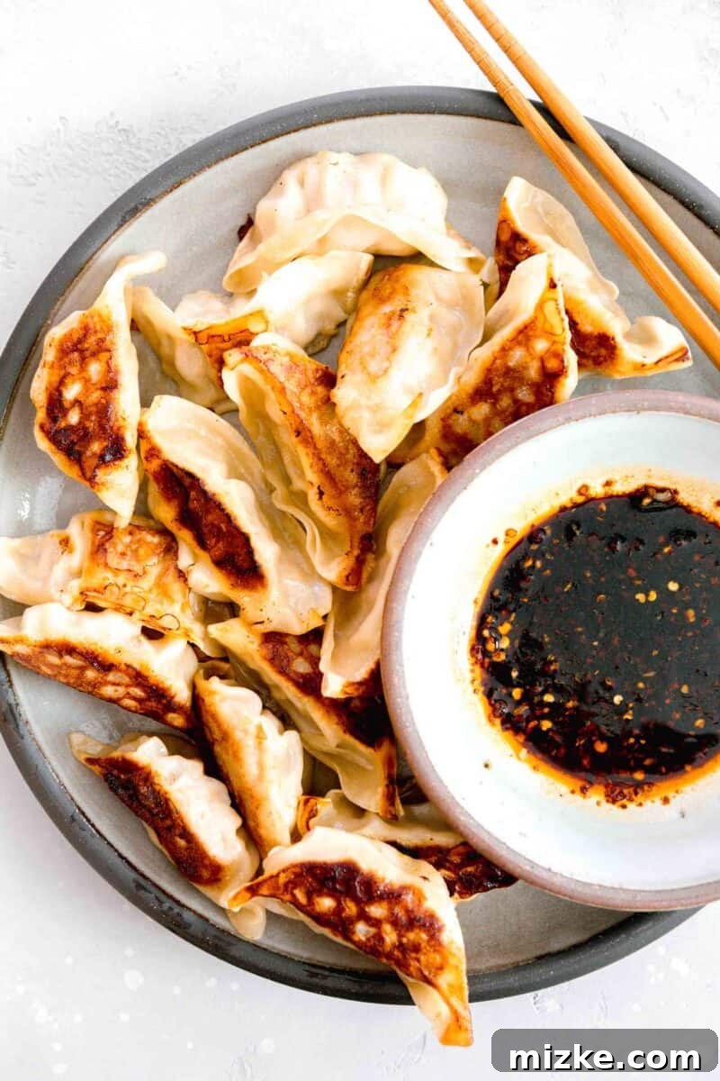 Your New Favorite Dumpling Sauce 2 Overhead view of perfectly pan-fried dumplings arranged beautifully on a grey ceramic plate, with a small bowl of rich, amber dumpling sauce resting invitingly beside them, accompanied by elegant wooden chopsticks.