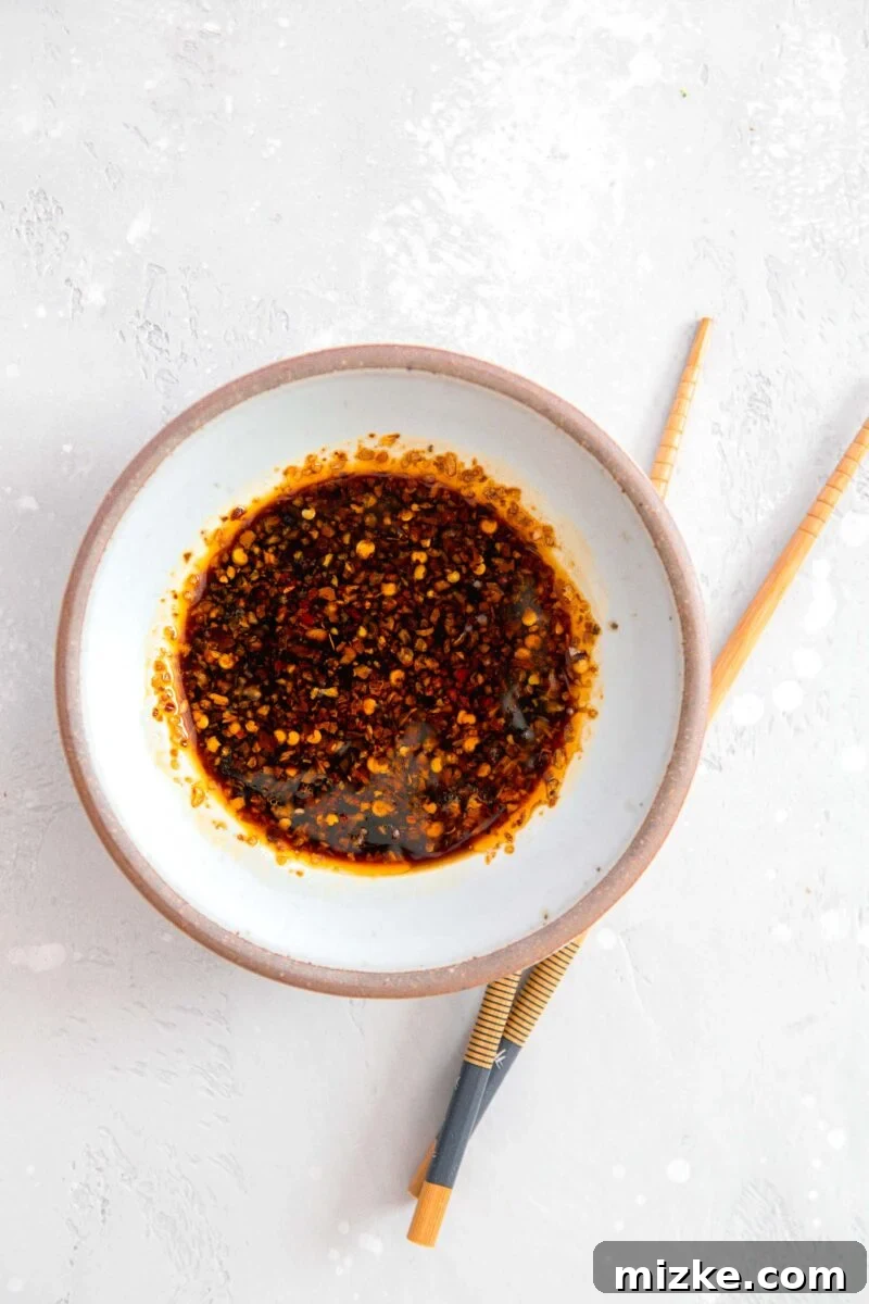Your New Favorite Dumpling Sauce 3 Close-up overhead shot of a small white ceramic bowl with an elegant brown rim, brimming with a rich, dark, and glossy homemade dumpling sauce. Wooden chopsticks rest invitingly beside the bowl, poised for the next delicious dip.
