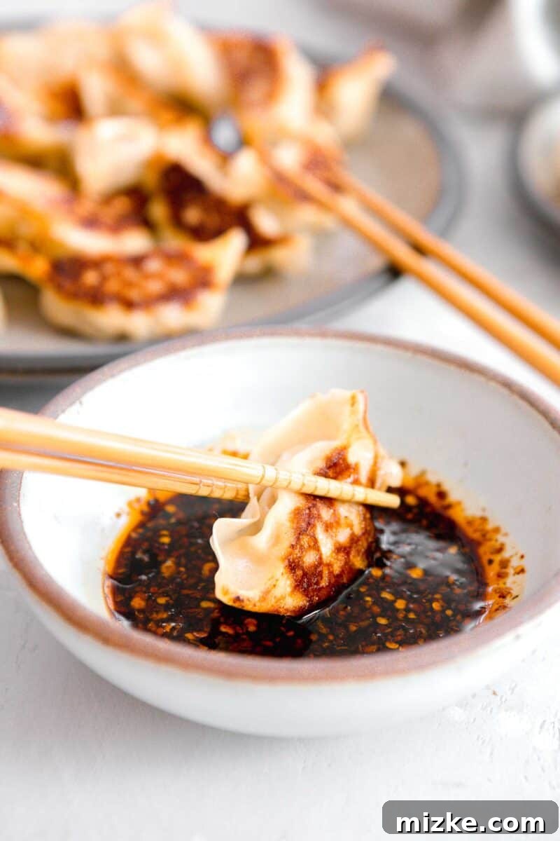 Your New Favorite Dumpling Sauce 6 A close-up action shot of a golden-brown, perfectly pan-fried dumpling being delicately dipped into the rich, dark, and glossy homemade dumpling sauce using a pair of elegant wooden chopsticks, ready for a delicious bite.