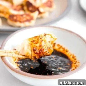 pan-fried dumpling dripping in dumpling sauce held onto by wooden chopsticks