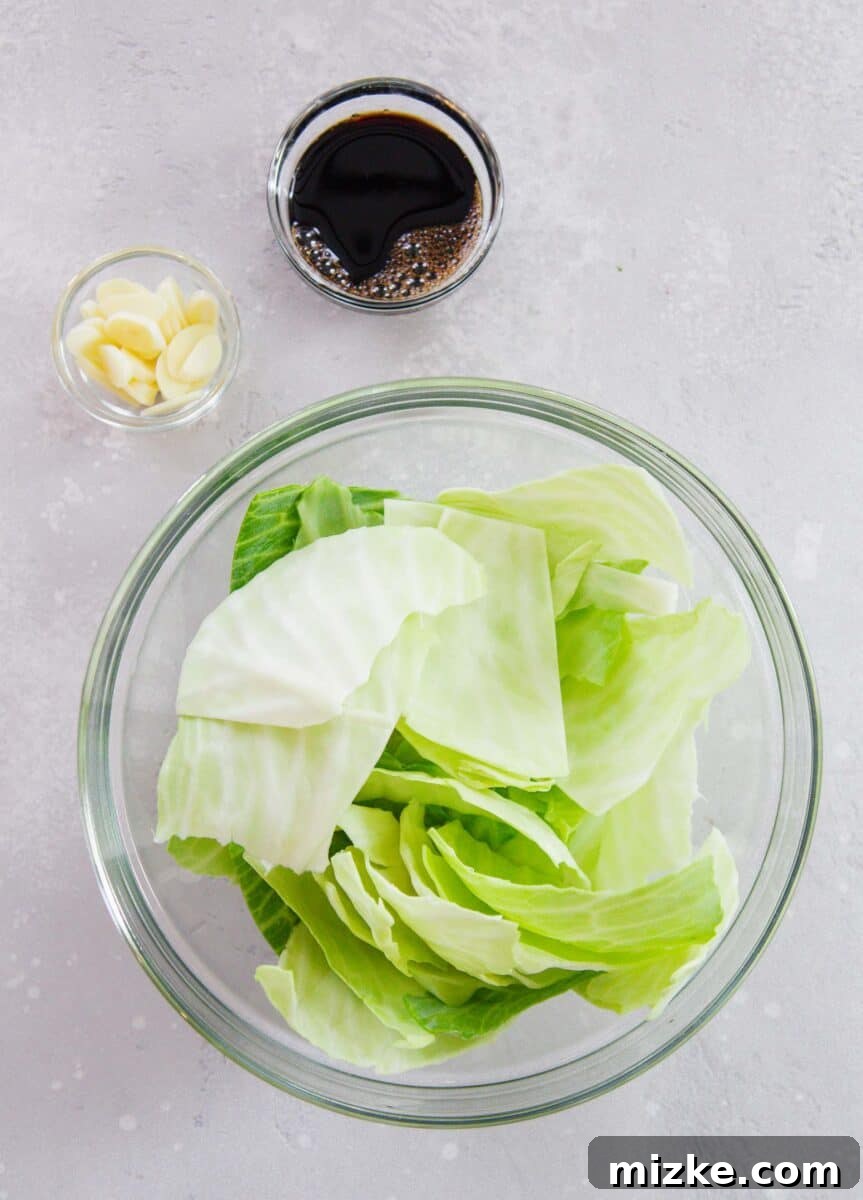 Key ingredients for Chinese cabbage stir fry: a head of green cabbage, a bulb of garlic, and a bottle of soy sauce, arranged on a wooden surface.