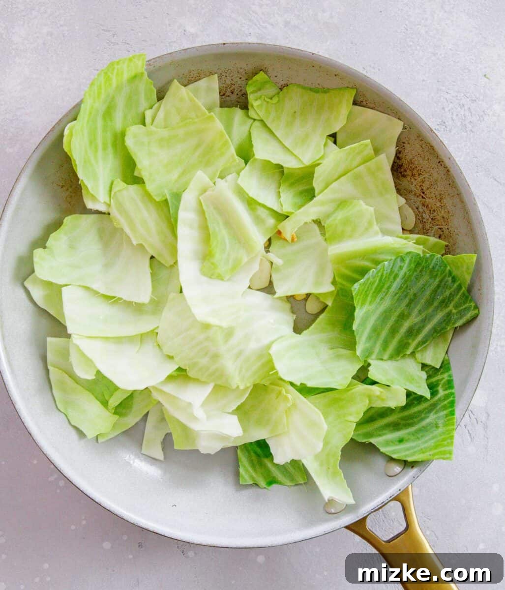 Roughly hand-torn green cabbage leaves added to a hot skillet with sautéed garlic slices, ready for stir-frying.