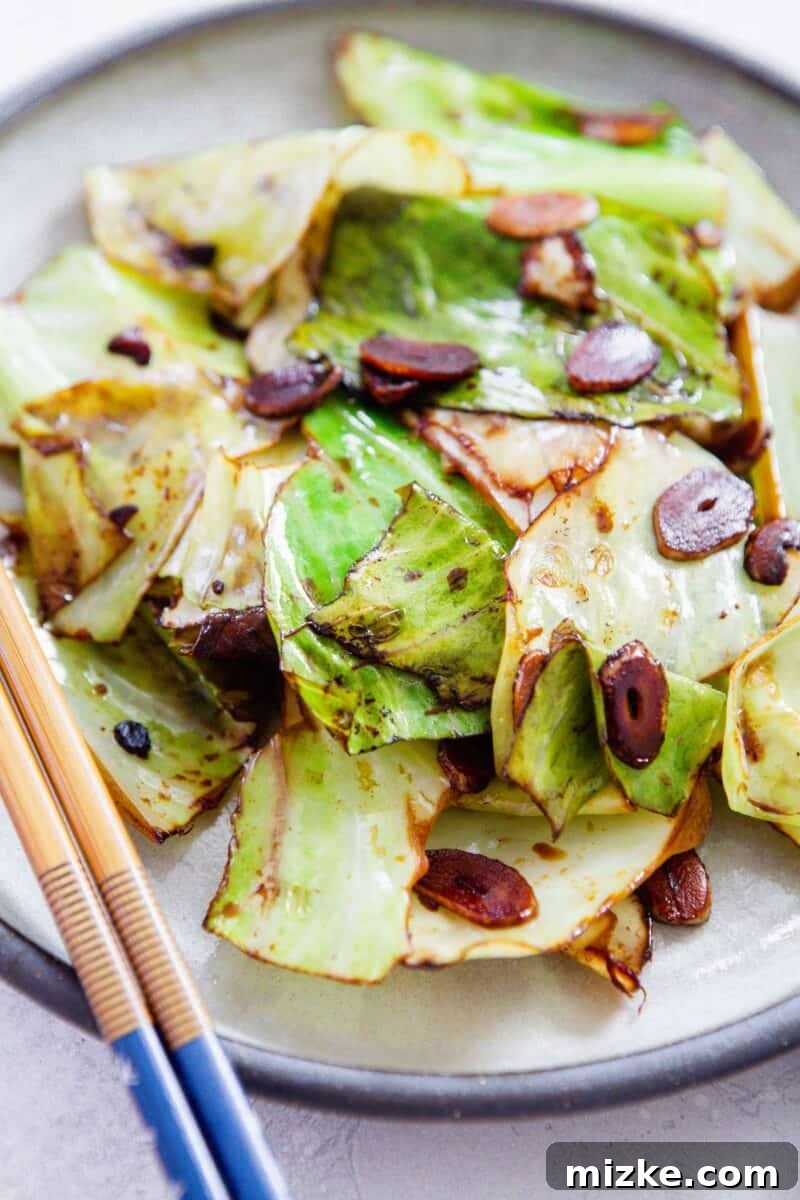 Close-up view of the finished Chinese cabbage stir fry, showcasing tender-crisp cabbage leaves glistening with soy sauce and interspersed with golden garlic slices on a white plate.