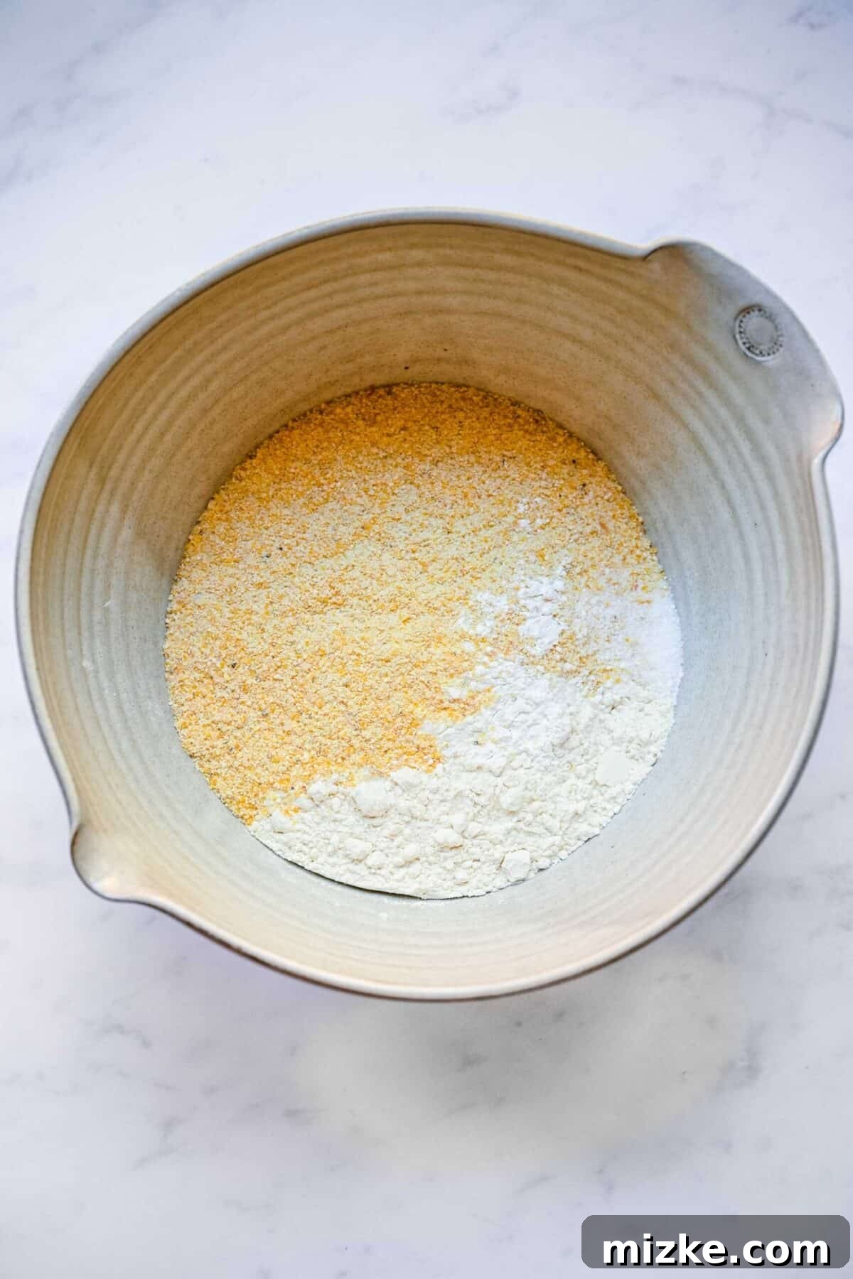 These cranberry maple cornbread muffins are incredibly moist, tender, sweet, and tart, making them an ideal side dish for Thanksgiving or Christmas gatherings. A mixing bowl holding a meticulously measured blend of flour, cornmeal, baking powder, and salt, ready for whisking.