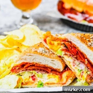 A close-up of the delicious layers of the grinder sandwich. Close up of a grinder sandwich cut in half, with a beer and a sandwich in the background