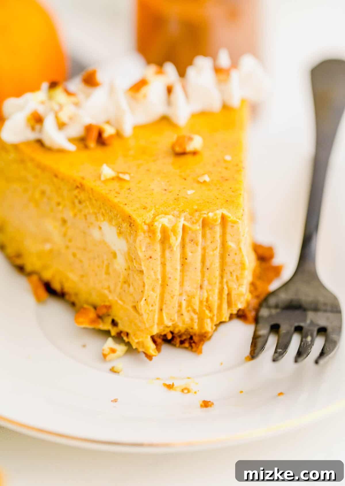 This easy pumpkin cheesecake recipe delivers a rich and creamy homemade experience, packed with authentic pumpkin flavor and swirled with comforting fall spices, making every bite a delight. A tantalizing close-up shot of a single slice of pumpkin cheesecake, with a perfect bite already taken, revealing its creamy texture and spiced filling. A fork rests invitingly beside the cake, ready for the next delicious mouthful, emphasizing its irresistible appeal.
