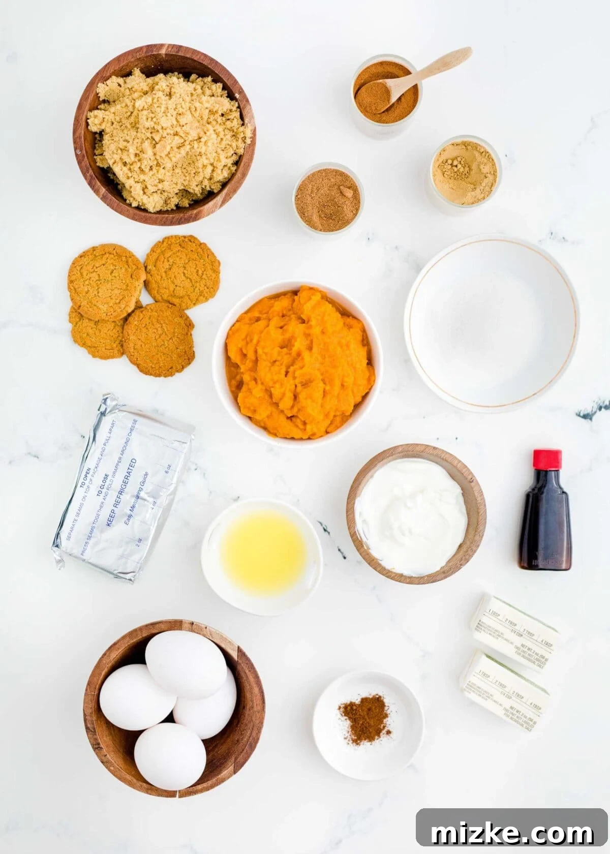 This easy pumpkin cheesecake recipe is celebrated for its rich and creamy homemade texture, packed with authentic pumpkin flavor and infused with a delightful mix of cozy fall spices, promising a delightful baking experience. An overhead shot showcasing all the essential ingredients laid out neatly for making a pumpkin cheesecake: bowls of brown sugar, white sugar, rich pumpkin puree, melted butter, eggs, individual bowls of various spices, a generous dollop of sour cream, a package of cream cheese, butter sticks, pure vanilla extract, and a pile of gingersnap cookies ready for the crust, illustrating the fresh, high-quality components.