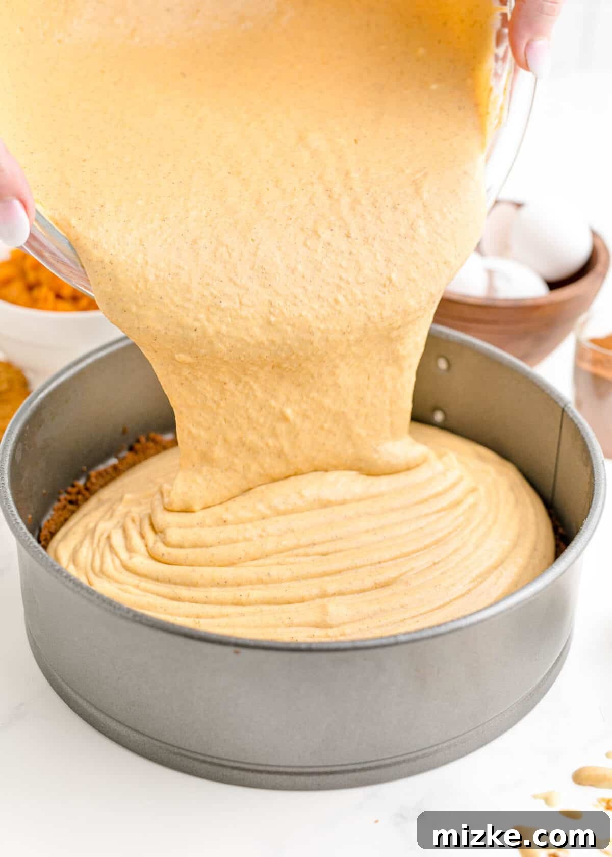This easy pumpkin cheesecake recipe yields a wonderfully rich and creamy homemade cheesecake, brimming with real pumpkin and infused with cozy fall spices, poured into its crust. Rich pumpkin cheesecake batter being carefully poured from a mixing bowl into the pre-baked gingersnap crust in a springform pan, demonstrating a key step in preparing this delicious fall dessert.
