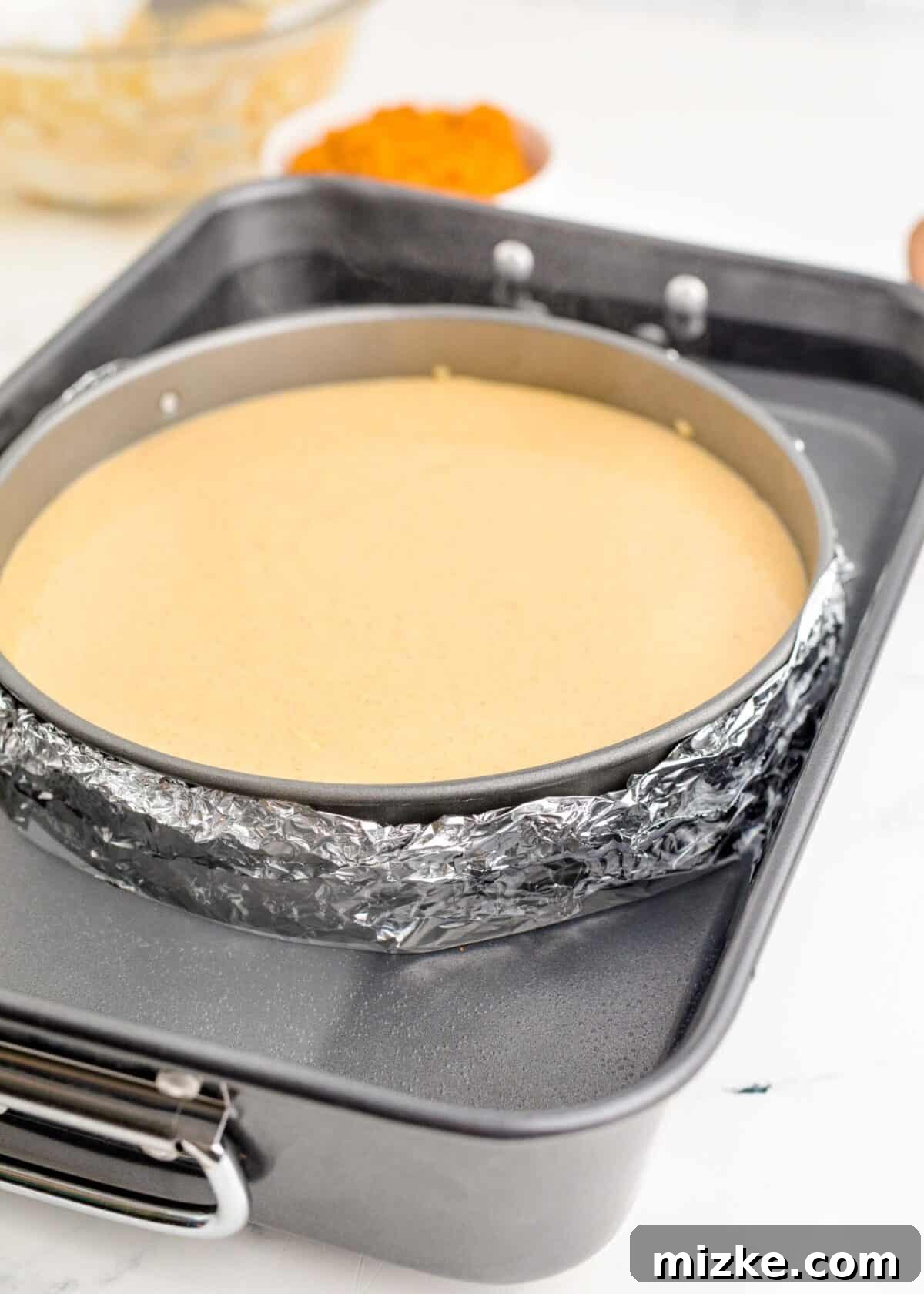 This easy pumpkin cheesecake recipe promises a rich and creamy homemade cheesecake, perfectly balanced with real pumpkin and a delightful swirl of cozy fall spices, prepared for its water bath. A springform pan, securely wrapped in a double layer of heavy-duty aluminum foil to prevent water seepage, filled with smooth pumpkin cheesecake batter and carefully placed inside a larger roasting pan for a water bath, ready for baking to achieve a perfect texture.
