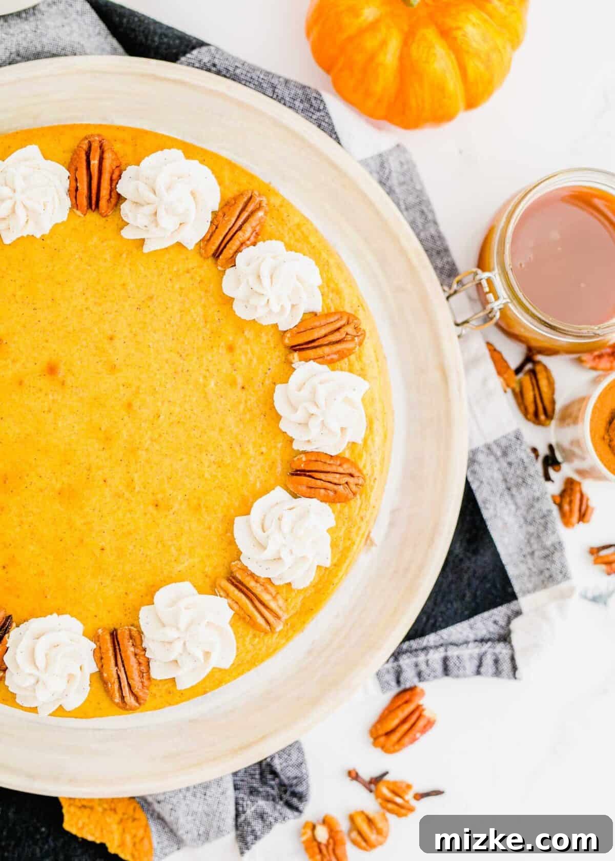 This easy pumpkin cheesecake recipe consistently delivers a rich and creamy homemade cheesecake, abundant with authentic pumpkin flavor and perfectly swirled with comforting fall spices, making it an ideal holiday treat. A close-up, partial view of a fully baked and chilled pumpkin cheesecake, exquisitely topped with delicate dollops of freshly whipped cream and crunchy pecans, ready to be enjoyed as a festive fall dessert.