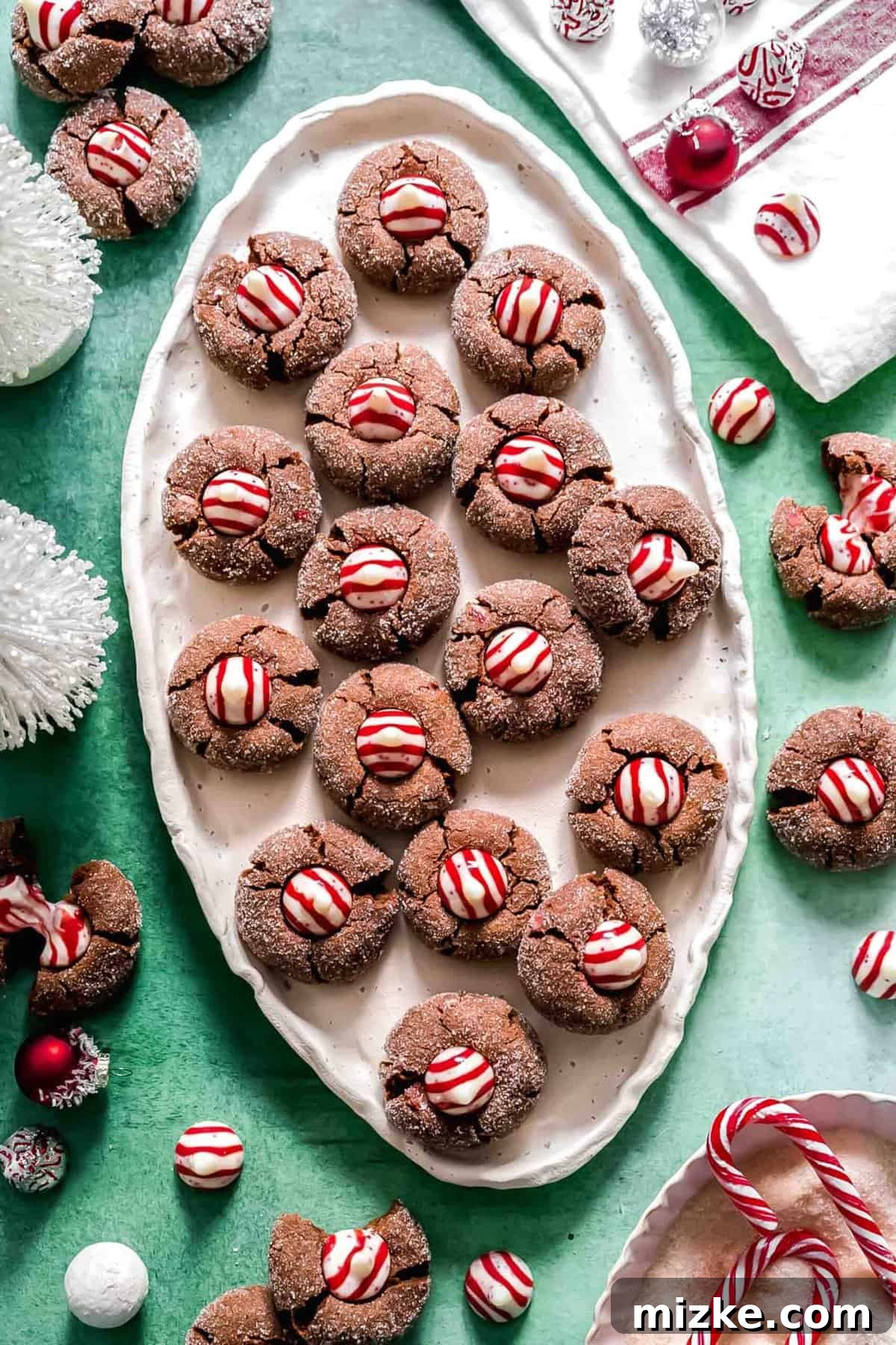 These chocolate peppermint kiss cookies are festive treats for Christmas, easy to make, and topped with a Hershey's candy cane kiss. An oval tray filled with beautifully arranged chocolate peppermint kiss cookies, surrounded by a scatter of unwrapped Hershey's peppermint kisses, ready for festive enjoyment.