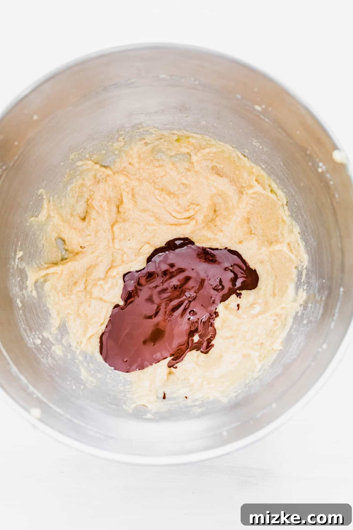 These chocolate peppermint kiss cookies are festive treats for Christmas, easy to make, and topped with a Hershey's candy cane kiss. A mixing bowl featuring creamed butter and sugars, with the melted chocolate pooled on top, ready to be blended into the wet mixture.