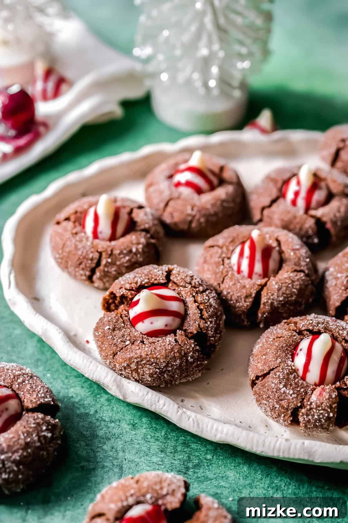These chocolate peppermint kiss cookies are festive treats for Christmas, easy to make, and topped with a Hershey's candy cane kiss. A close-up shot of a beautifully arranged plate filled with chocolate peppermint kiss cookies, ready to be served and enjoyed during the festive season.