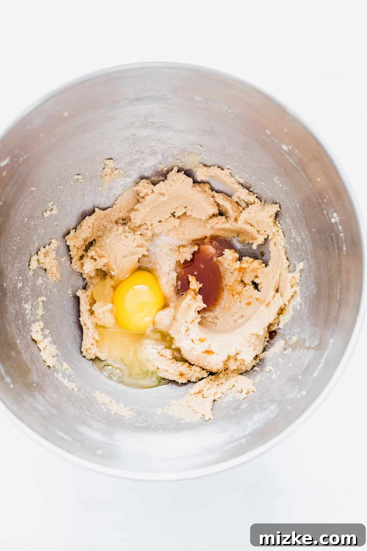 These chocolate peppermint kiss cookies are festive treats for Christmas, easy to make, and topped with a Hershey's candy cane kiss. A mixing bowl showing the perfectly creamed butter and sugars, topped with an egg, vanilla extract, and peppermint extract, awaiting incorporation into the dough.